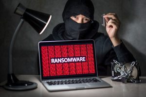 Hacker with computer screen showing ransomware attacking, alert in red digital binary background with hard disk drive lock. Cyber attack concept
