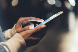 close-up image of male hands using smartphone at night on city shopping street, searching or social networks concept, hipster man typing an sms message to his friends
